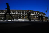 Runners pass by Japan National Stadium, where opening ceremony and many other events are planned for postponed Tokyo 2020 Olympics, Thursday, Jan. 21, 2021, in Tokyo. The postponed Tokyo Olympics are to open in just six months. Local organizers and the International Olympic Committee say they will go ahead on July 23. But it’s still unclear how this will happen with virus cases surging in Tokyo and elsewhere around the globe. (AP Photo/Kiichiro Sato)