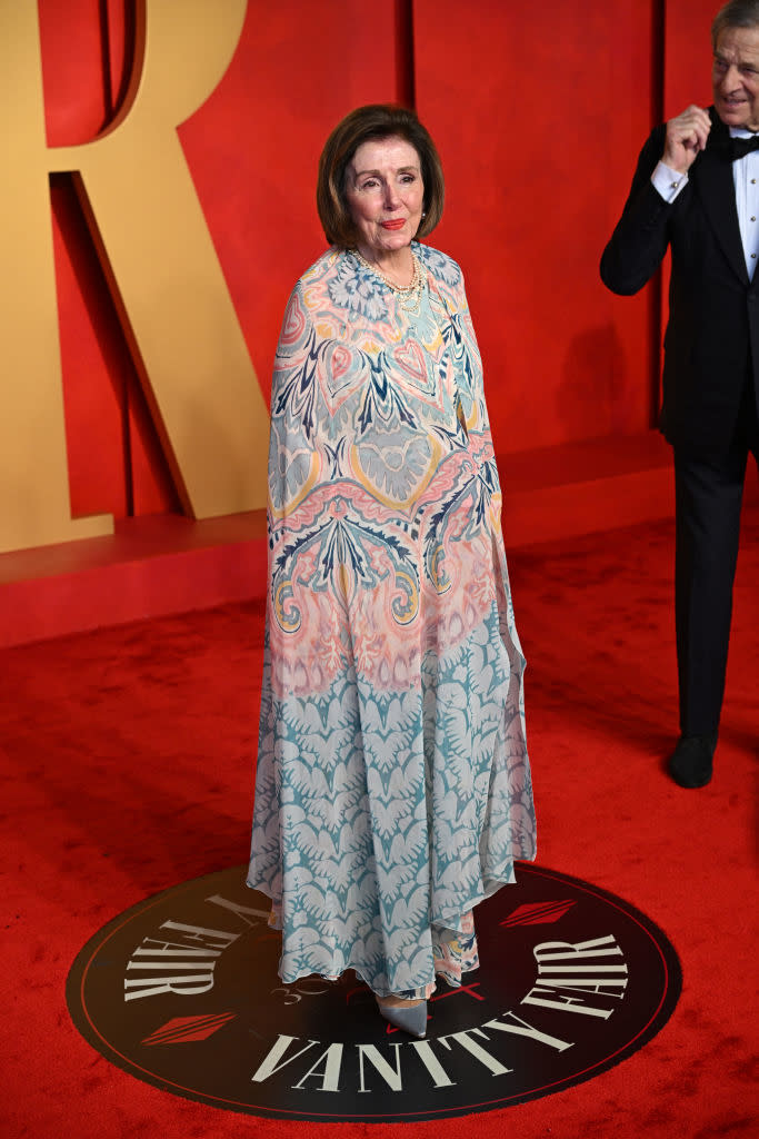 Woman in patterned gown at Vanity Fair event; man partially visible in background