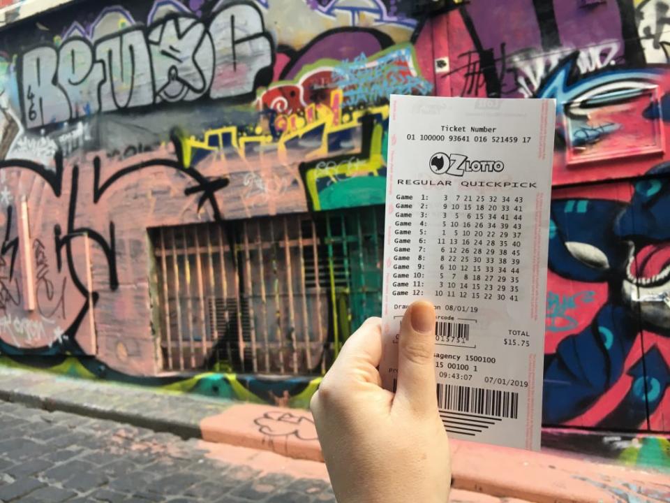 A person holds an Oz Lotto ticket in a Melbourne laneway.