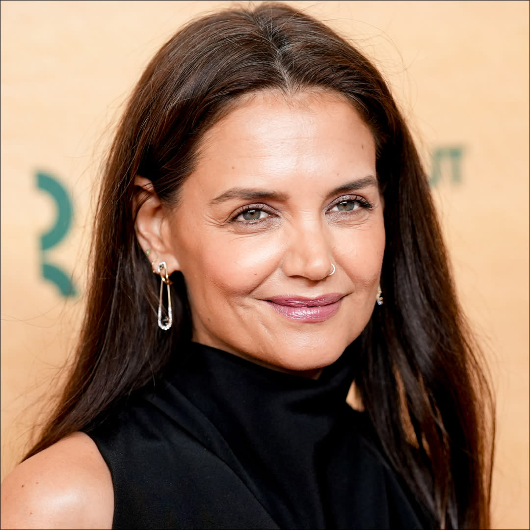  Katie Holmes in front of a plain backdrop on a red carpet. 