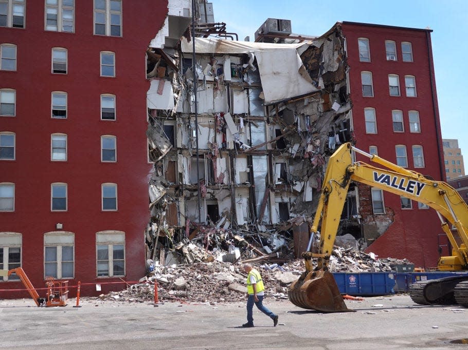 the center portion of a six-story red apartment building collapsed in Davenport, Iowa. The debris sits on the ground with a bulldozer in front