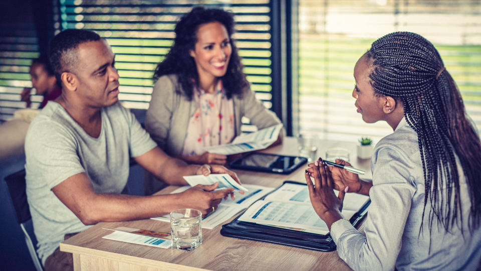 Couple of African descent sitting at the table with their financial advisor talking about loan options.