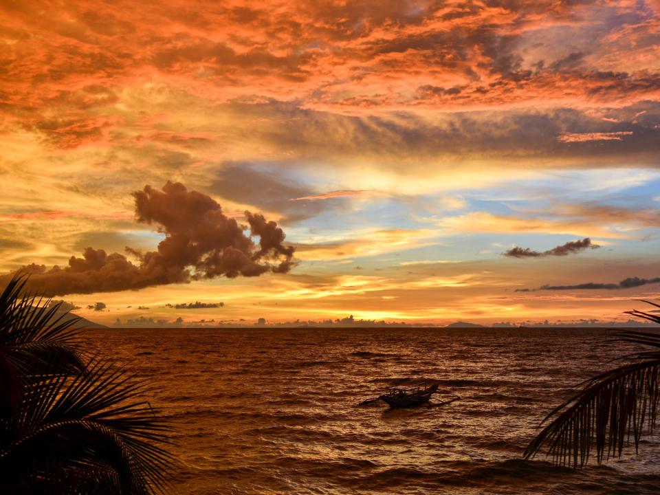 A traditional fishing boat is moored off shore during a sunset in the Philippines.