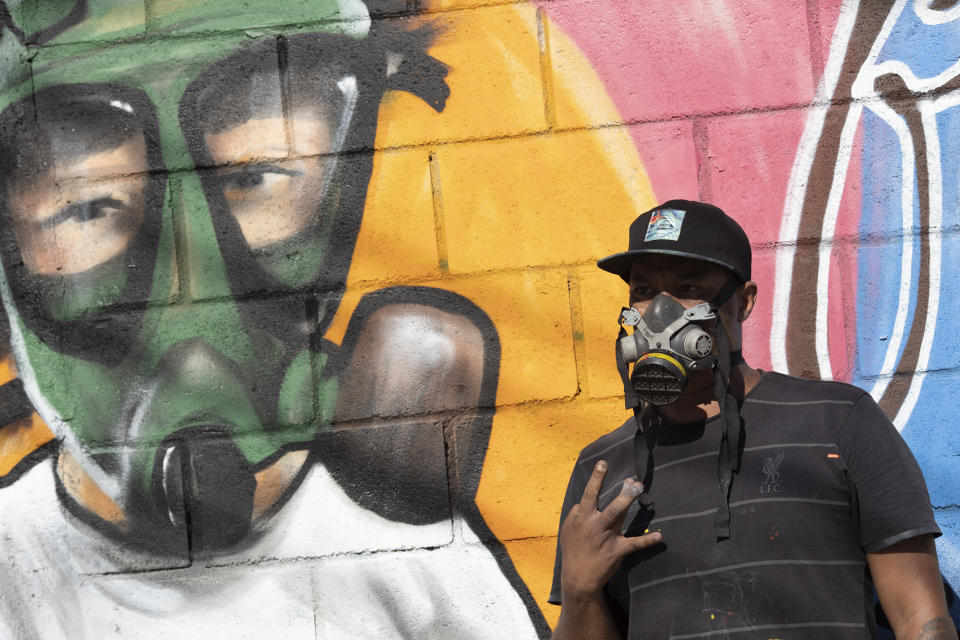 Graffiti artist Angelo Campos poses for a photo by his mural referencing the COVID-19 pandemic which he said he painted in honor of health workers in Rio de Janeiro, Brazil, Thursday, May 21, 2020. Campos, 39, has lost two relatives to the new coronavirus. (AP Photo/Silvia Izquierdo)