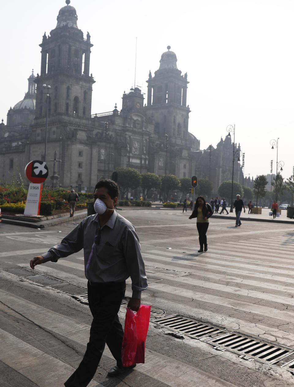 A man wearing a face mask crosses a street by the Metropolitan Cathedral, shrouded by haze, in the Zocalo, Mexico City's main square, Thursday, May 16, 2019. A siege of air pollution blanketing the capital has led to school closures and the cancellation of professional sporting events. (AP Photo/Rebecca Blackwell)