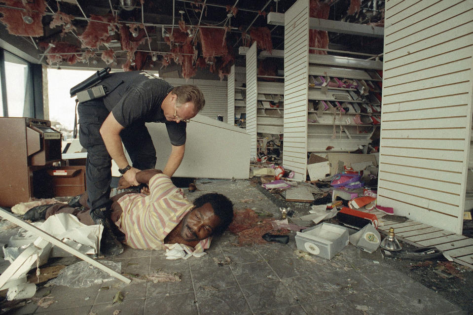 <p>Homestead Police Officer Harley Foust puts on handcuffs as he arrests Anthony Minnis inside a destroyed Payless Shoe store in Homestead, Aug. 26, 1992, after Minnis was found inside the store. Police and National Guard troops patrolled against looting in Dade County Wednesday as a dusk-to-dawn curfew remained in effect. (AP Photo/David Bergman) </p>