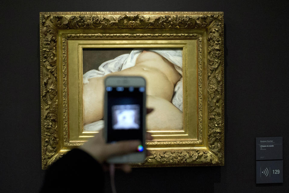 CORRECTS YEAR TO 1866, NOT 1966-FILE - In this Feb. 12 2016 file photo, a visitor takes a picture of Gustave Courbet's 1866 "The Origin of the World," at Musee d'Orsay museum, in Paris. She was a courtesan living from subsidies provided by rich men - but preferring the company of women - and ended her life as a very honorable patroness helping orphans. Mademoiselle Constance Queniaux was 34 in 1866 when the French master Gustave Courbet painted her in L’Origine du monde (The Origin of the World), a realistic close up of a woman's naked torso, legs spread and face hidden by a rumpled sheet. French literature expert Claude Schopp found by chance the mention of her name in a letter by French writer Alexandre Dumas fils, the son of The Three Musketeers’ author. (AP Photo/Francois Mori, File)