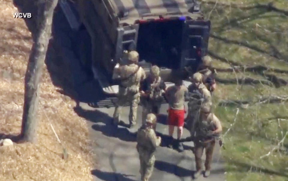 FBI agents arrest Jack Teixeira, who is wearing red shorts, and walk him to a van.