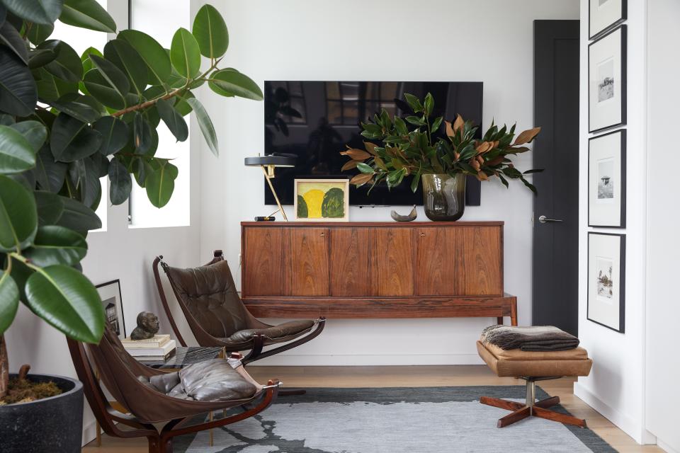 The vintage Falcon chairs are by Norweigian designer Sigurd Resell, and the rosewood cabinet is by Danish furniture designer Arne Vodder. The desk lamp is by Dutch designer Louis Klaff, and the painting by Venezulan contemporary artist Alvaro Barrington. To the left is a bronze head by contemporary artist Stefan Bassir, which Basmajian received as a birthday gift. The carpet is from Christopher Farr, and the vintage stool is in rosewood. The photographs are called Desert Houses, by American artist Mark Ruwedel.