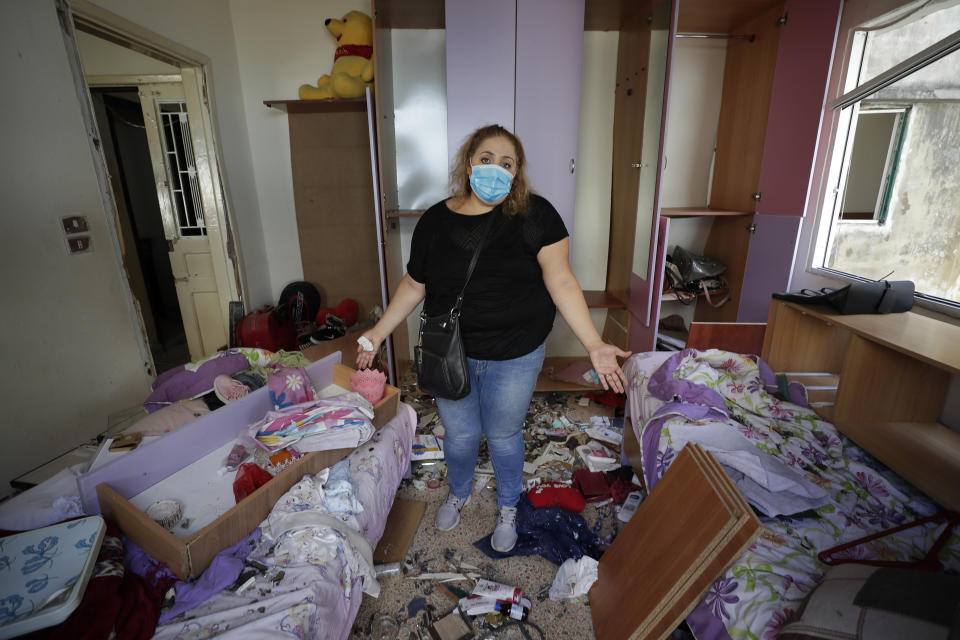 Mona Al Chami, poses for a photograph inside her destroyed apartment after Tuesday's explosion in the seaport of Beirut, Lebanon, Thursday, Aug. 6, 2020. The gigantic explosion in Beirut on Tuesday tore through homes, blowing off doors and windows, toppling cupboards, and sent flying books, shelves, lamps and everything else. Within a few tragic seconds, more than a quarter of a million people of the Lebanese capital's residents were left with homes unfit to live in. Around 6,200 buildings are estimated to be damaged. (AP Photo/Hassan Ammar)