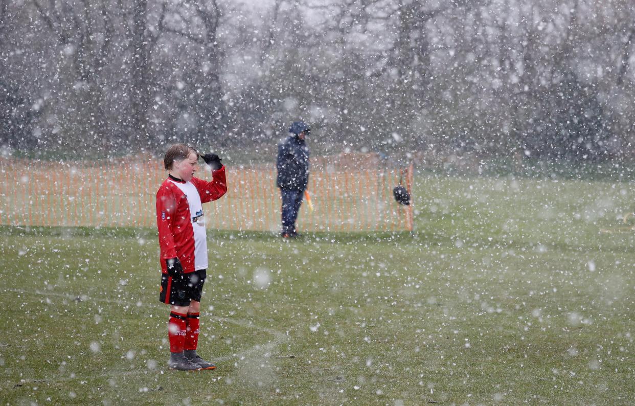 A young footballer shields his eyes during an unexpected snow storm in Altrincham, UK, on 10 April, 2021.  (REUTERS)