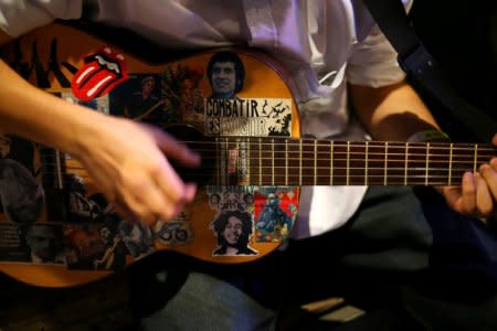 A man plays a guitar with an image of Victor Jara (top) during