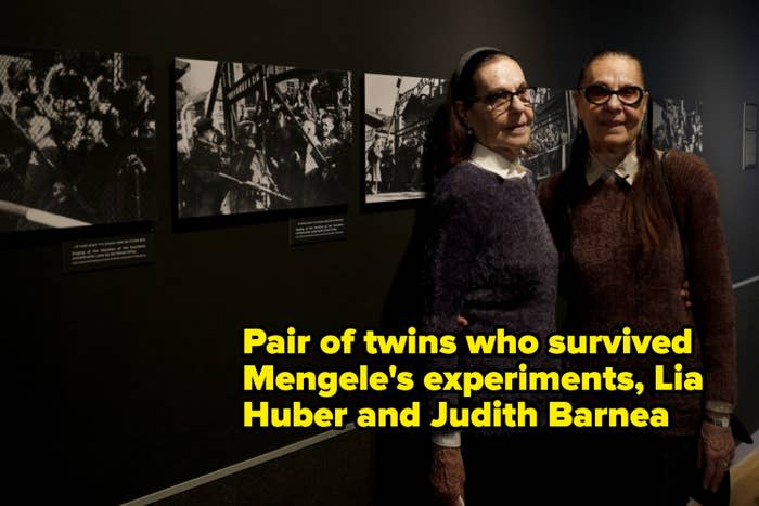 Two women with similar looks stand side by side in front of a wall displaying black-and-white historical photos at an exhibition