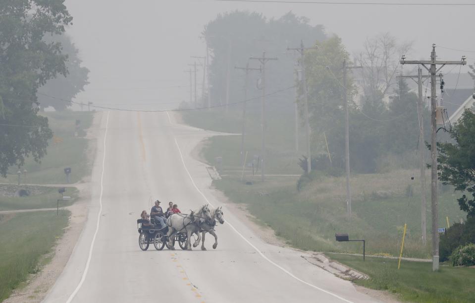 Under hazy skies, John and Jenny Petrie take their grandchildren and daughter-in-law Katie Petrie for a horse and carriage ride Tuesday, June 27, 2023, along County BB in the Town of Chilton, Wis.