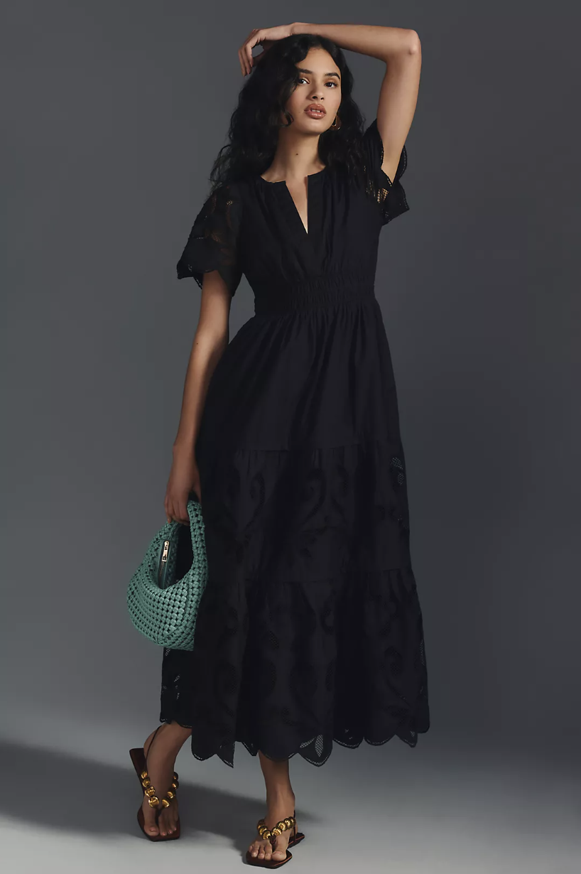 brunette model wearing sandals, green braided bag and The Somerset Maxi Dress: Cutwork Edition in black (photo via Anthropologie)