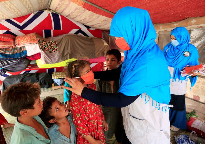 FILE PHOTO: A UNICEF worker helps an internally displaced girl put on a face mask at a makeshift camp, amid the coronavirus disease (COVID-19) outbreak, in Jalalabad