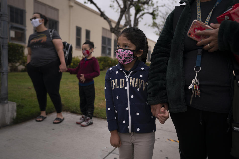 Francisca Valenzuela, 7, accompanied by her mother, waits to check in on the first day of in-person learning at Heliotrope Avenue Elementary School in Maywood, Calif., Tuesday, April 13, 2021. More than a year after the pandemic forced all of California's schools to close classroom doors, some of the state's largest school districts are slowly beginning to reopen this week for in-person instruction. (AP Photo/Jae C. Hong)