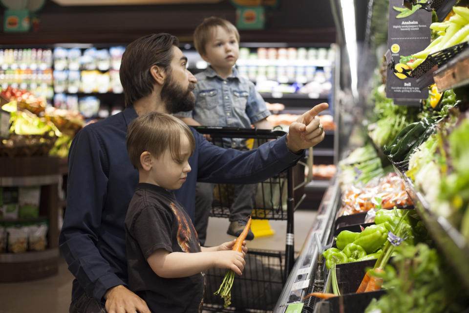 Father grocery shopping with his two children browsing organic vegetable section.