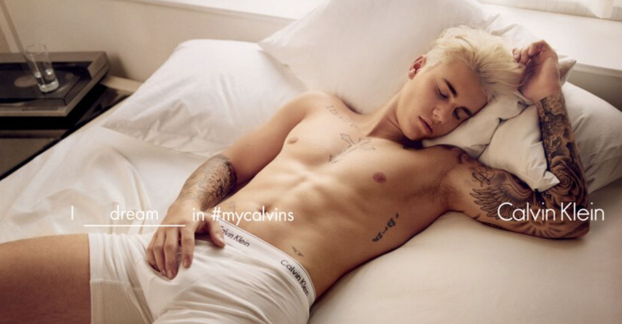 A tatted Justin Bieber in his Calvins lying on a bed with eyes closed.