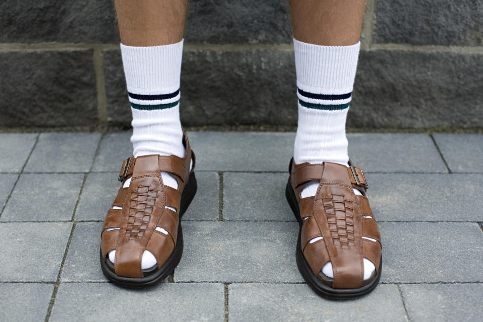 A man's legs from mid-calf down, wearing high white socks with two stripes and brown leather sandals