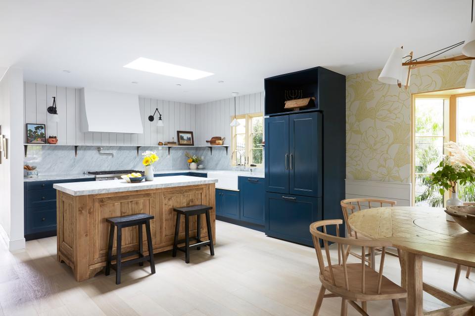 AFTER: The floor plan was opened up to make the kitchen feel more spacious. Custom wallpaper was added to the kitchen, as well as farmhouse aesthetics such as wood paneling and bright windows.