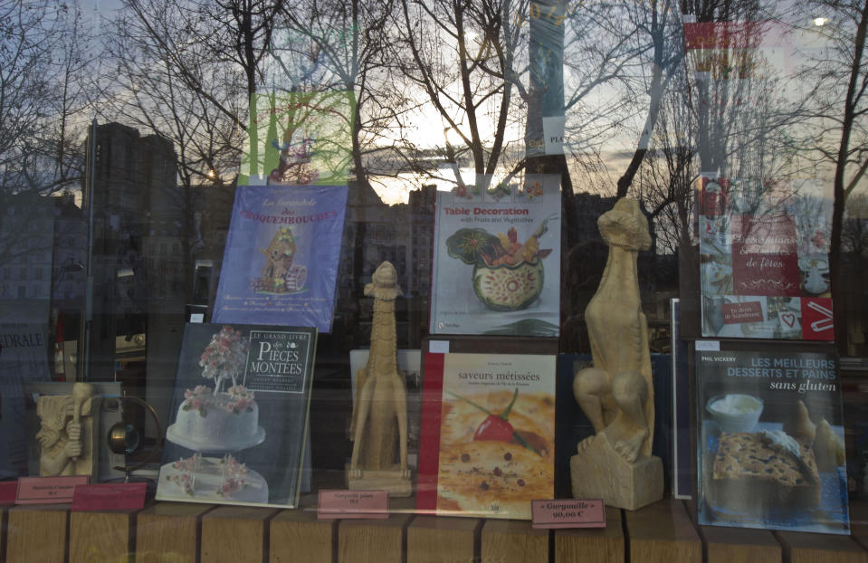 In this Wednesday, Jan. 8, 2014 photo, the Notre Dame cathedral, left, reflects in a window shop with cooking books on display between replicas of Notre Dame's gargoyle sculptures in Paris. You can start your walk on the Rue Saint-Jacques, which begins across the street from the restaurant Les Papilles and will take you all the way to the Seine, over a bridge to Ile de la Cite and to the plaza in front of Notre Dame cathedral. The facade has been cleaned recently for the church's 850th anniversary, and it is particularly stunning at night. (AP Photo/Michel Euler)