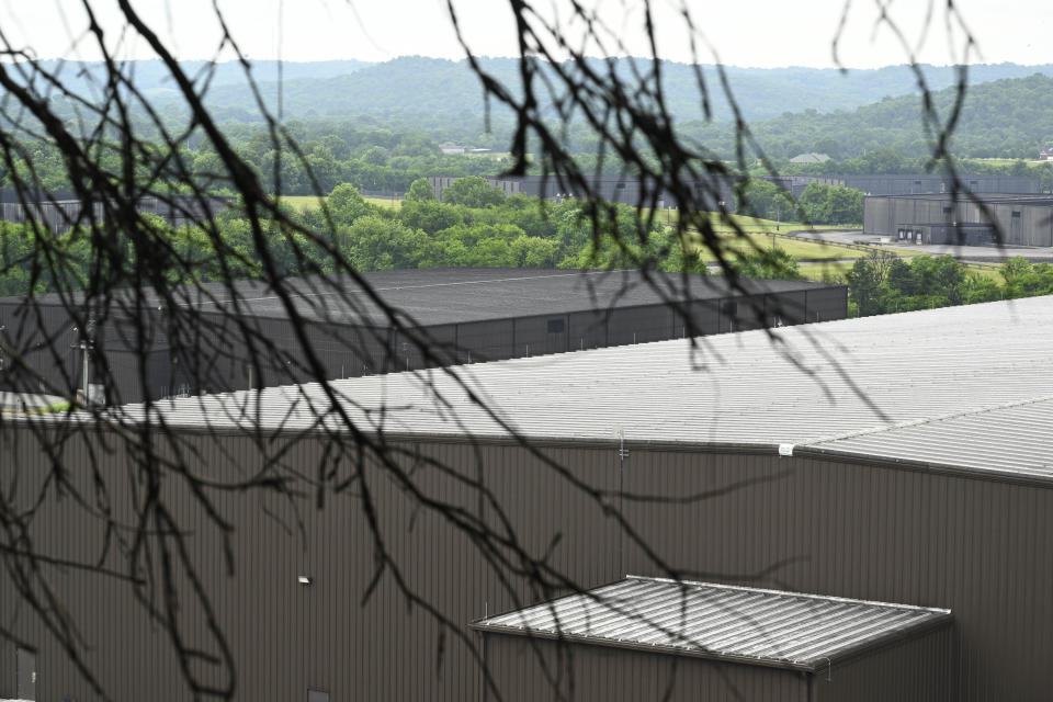 A newer Jack Daniels barrelhouse, front right, sits next to an older one, which has a roof covered in black substance, Wednesday, June 14, 2023, in Mulberry, Tenn. A destructive and unsightly black fungus, seen growing on dead tree limbs in the foreground, feeds on ethanol emitted by whiskey barrels and has been found growing on property near the barrelhouses. (AP Photo/John Amis)