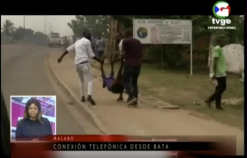 This TVGE image made from video shows people carrying a victim away after a blast site at a military barracks in Bata, Equatorial Guinea, Sunday, March 7, 2021. A series of explosions killed at least 20 people and wounded more than 600 others on Sunday, authorities said. (TVGE via AP)