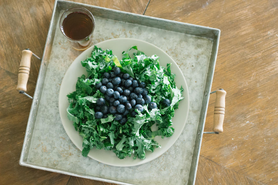 kale salad with blueberries and a glass of tea on an old serving plate