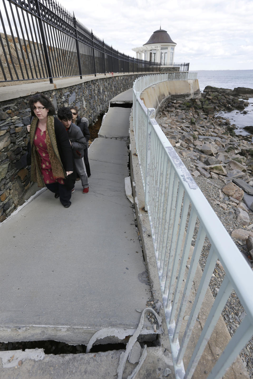 FILE - In this Wednesday, March 27, 2013 file photo, Jeanine Chada, of New York, front left, makes her way along a sunken and damaged portion of the Cliff Walk, in Newport, R.I. Large portions of the Cliff Walk damaged by Superstorm Sandy have yet to be repaired as the summer tourist season approaches. (AP Photo/Steven Senne, File)