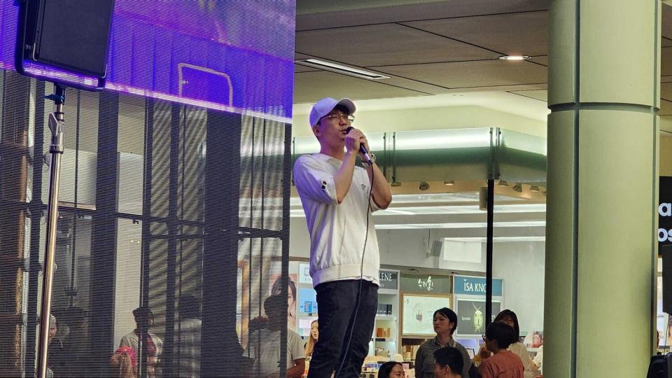 A man in a baseball cap sings karaoke onstage.