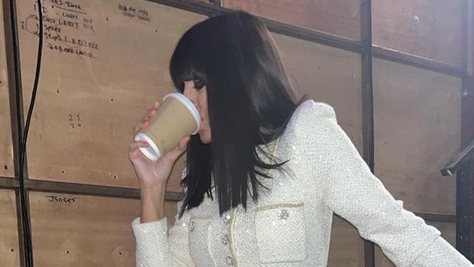 Claudia Winkleman poses backstage at Strictly wearing a bejewelled Self-Portrait dress. She is holding a brown coffee cup. 