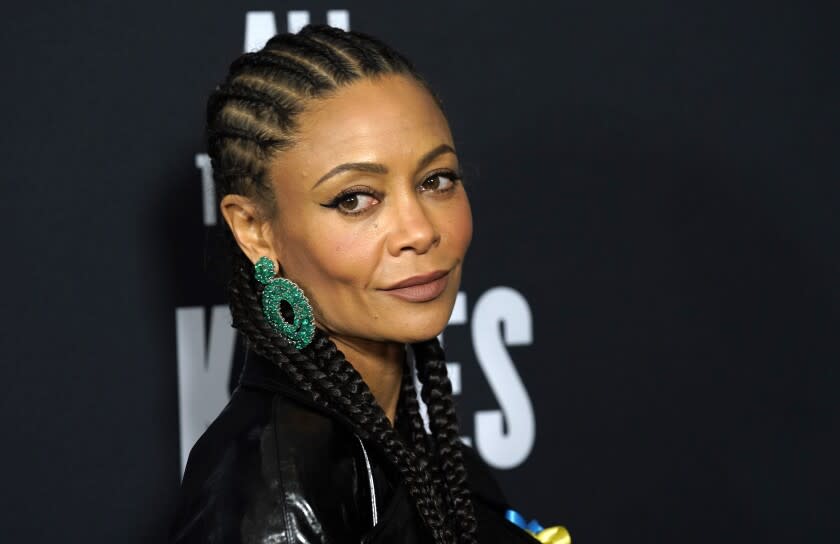 A woman with braided hair and large green earrings looks out of the corner of her eye