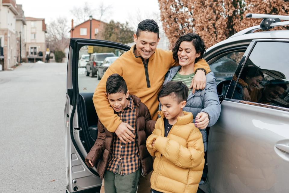 A family of four gather in front a car during colder months