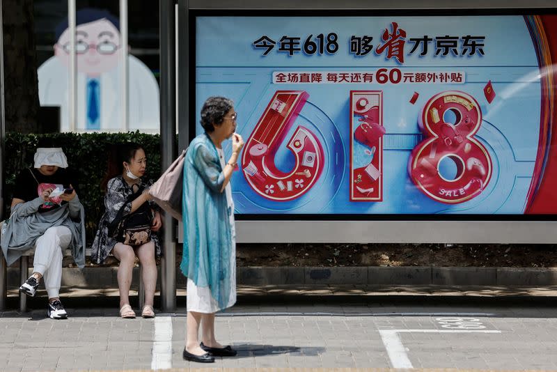 People wait for bus near a billboard of JD.com advertisement for the "618" shopping festival, in Beijing