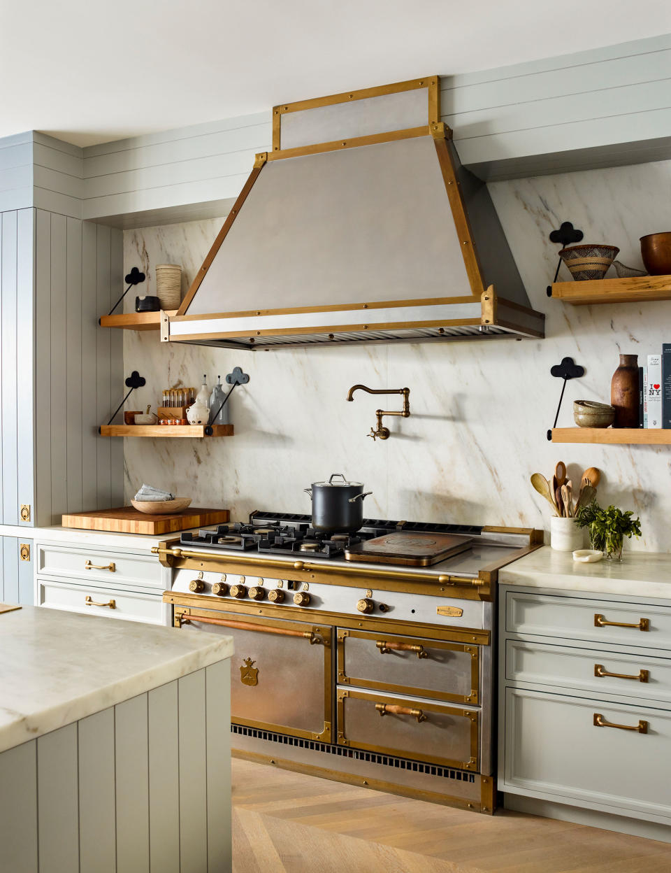 Modern kitchen with stainless steel range with gold detailing, marble backsplash and wood flooring