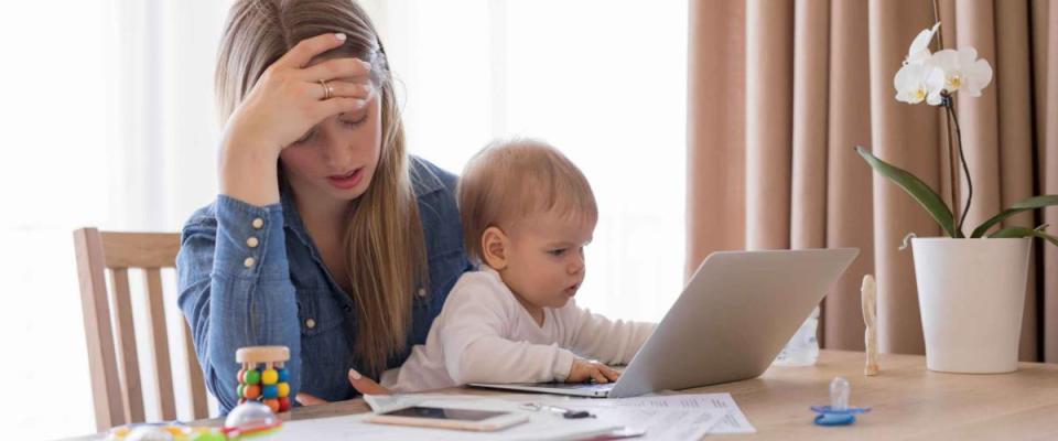 Tired working mom with child in her lap, head in hand and looking at bills on table