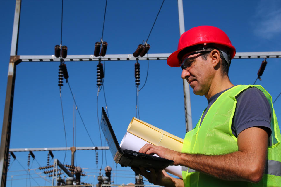 A man working on a computer with electric transmission equipment behind him