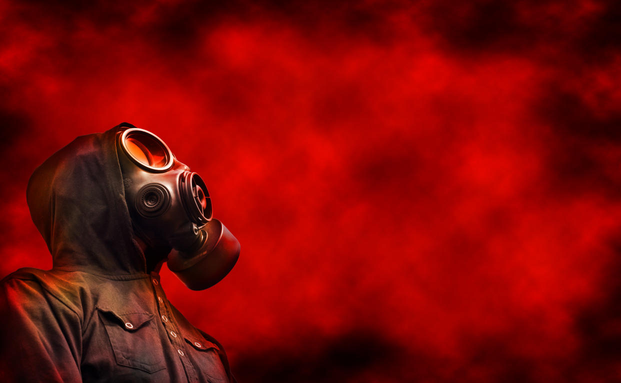 Person wearing hoody and gas mask with red toxic fumes