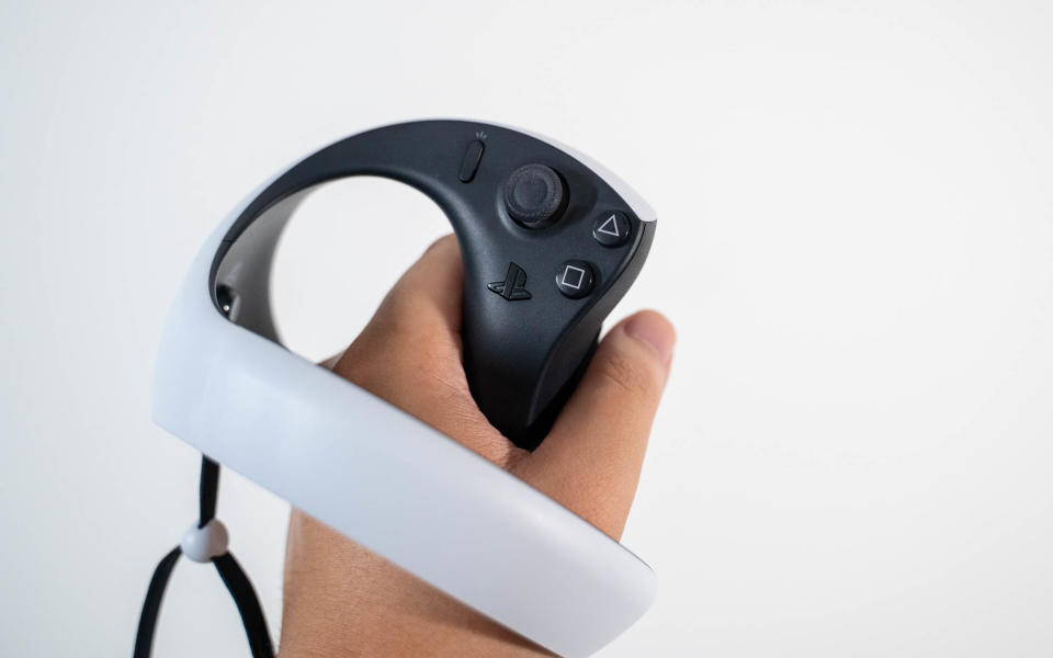 A white PlayStation VR2 Sense controller held by a hand.