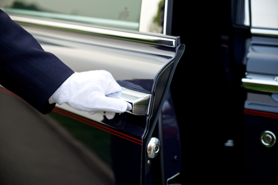 A gloved hand opens a car door, suggesting a luxurious or formal transportation service