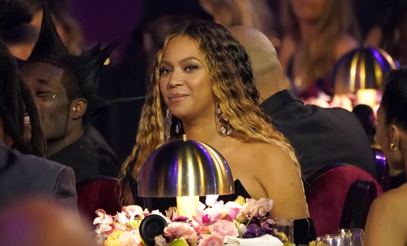 A woman with long brown hair sitting at a table with a lamp and floral bouquet in a crowd