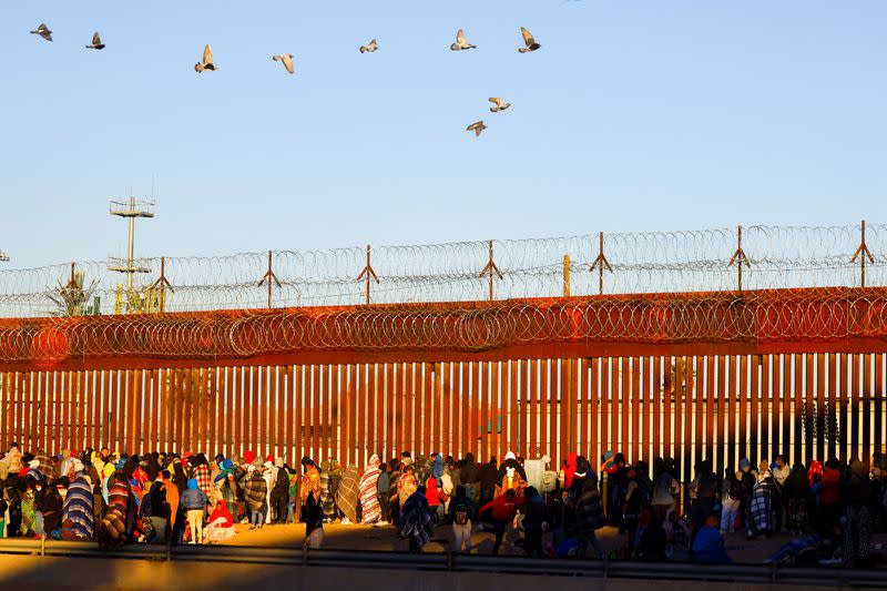 Migrants queue near the border wall after crossing the Rio Bravo river, in Ciudad Juarez