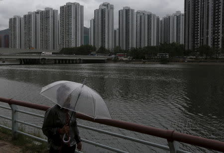 A passer-by walks along a riverside as City One Shatin residential precinct is seen at background in Hong Kong, China July 21, 2015. REUTERS/Bobby Yip