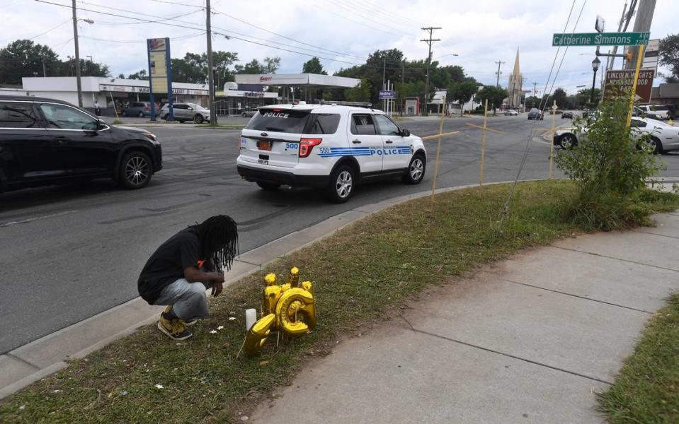 Timothy Moore kneels beside a memorial at the corner of Beatties Ford Road and Catherine Simmons Avenue on Tuesday, June 23, 2020, in memory of his cousins Christopher Antonio Gleaton, and Kelly Miller, two of the three people killed at an outdoor party the previous morning.