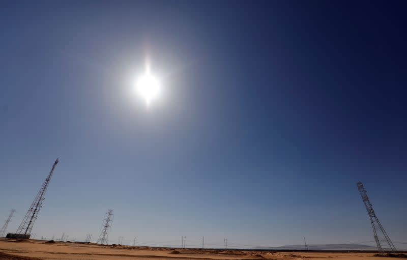 The sun shines over high-voltage power lines and electricity pylons at a highway front of the solar park of Benban plant in Aswan