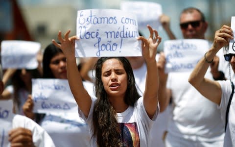 Followers of Joao Teixeira de Faria take part in a demonstration in Abadiania, Brazil. The sign reads: "We are with you, medium Joao." - Credit: REUTERS/Adriano Machado