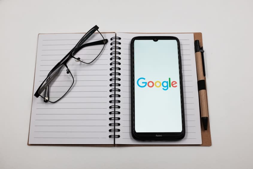  Google logo is displayed on a smartphone screen above a notebook next to glasses 