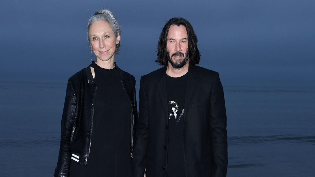 Keanu Reeves and Alexandra Grant hold hands on the beach, posing for cameras.