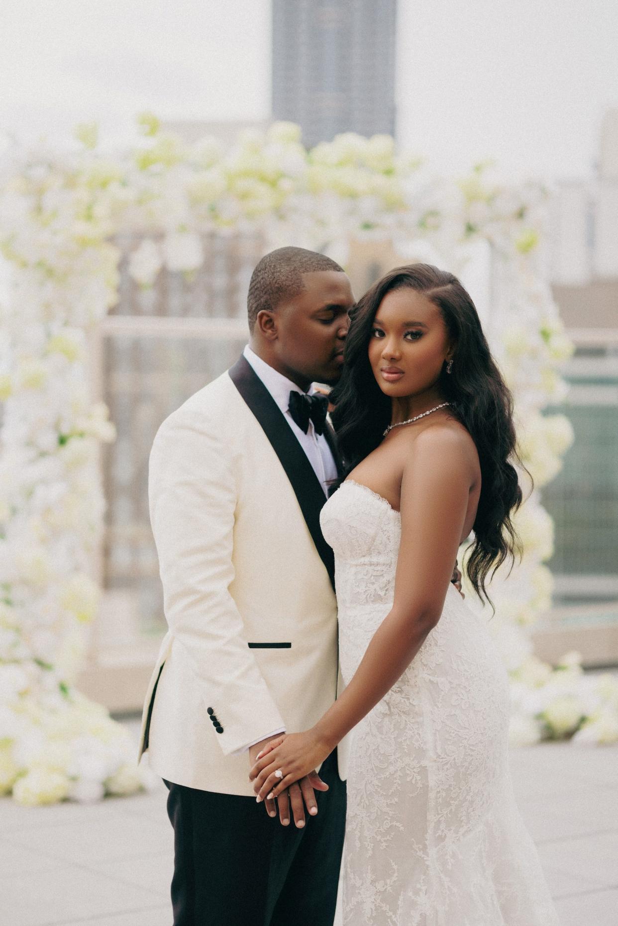 A bride and groom embrace, touching their hands.